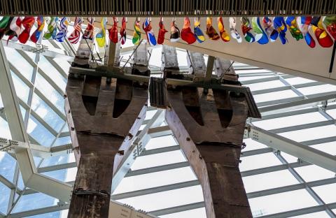 Two enormous rusty trident-looking structures emerge in a window-covered atrium. Multicolored flags from every nation hang down from the overhang that borders the photo.