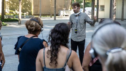 A tour guide speaks to a group of visitors, who appear from the back, on the Memorial plaza
