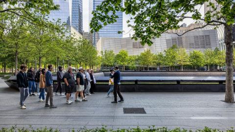 A group listens to a tour guide in front of a Memorial pool on the plaza