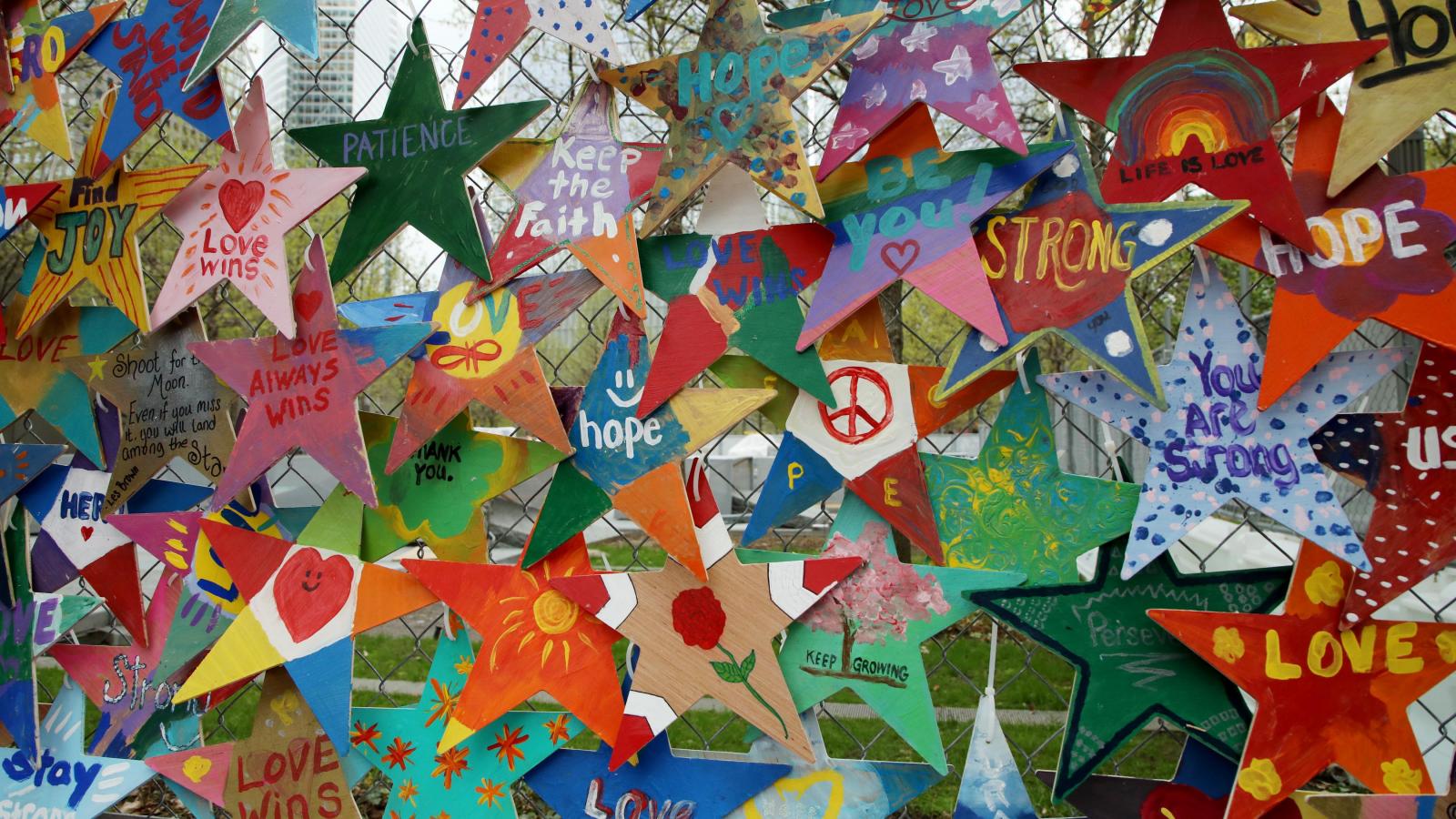 An array of hand-crafted Stars of Hope decorate a fence near the 9/11 Memorial plaza.  The stars bear messages such "Peace," "Keep the Faith," and "Love Wins."