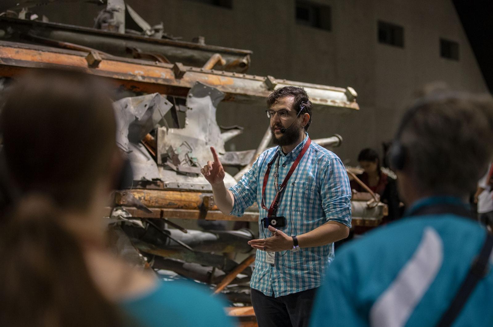 A male tour guide stands in front of the mangled antenna of Tower One as he talks to visitors on a guided tour in Memorial Hall.