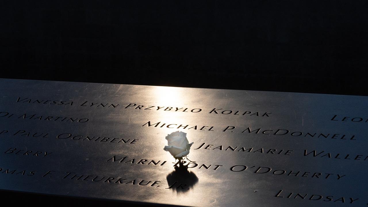 Soft light illuminates a single, white rose placed at a name etched on a bronze parapet of the Memorial.