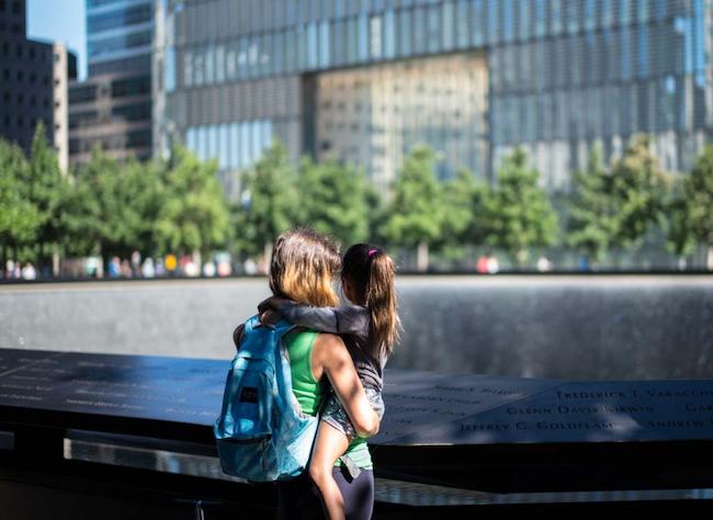 Back view of an adult holding a child on her hips looking at names on the Memorial
