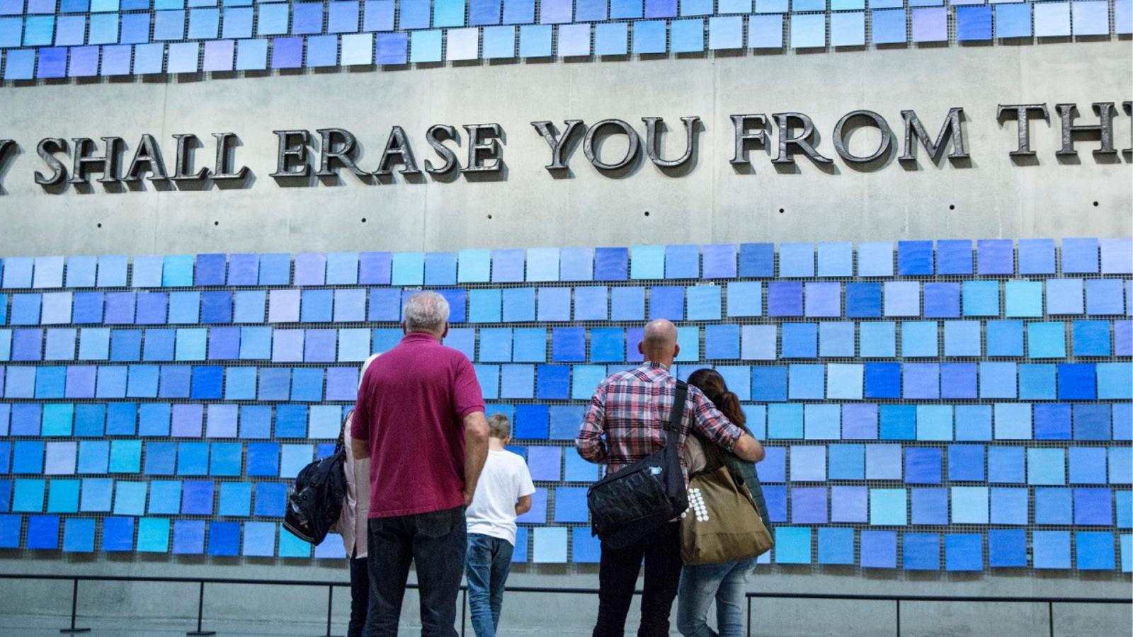 Patrons, seen from the back, look at a blue tiled art installation