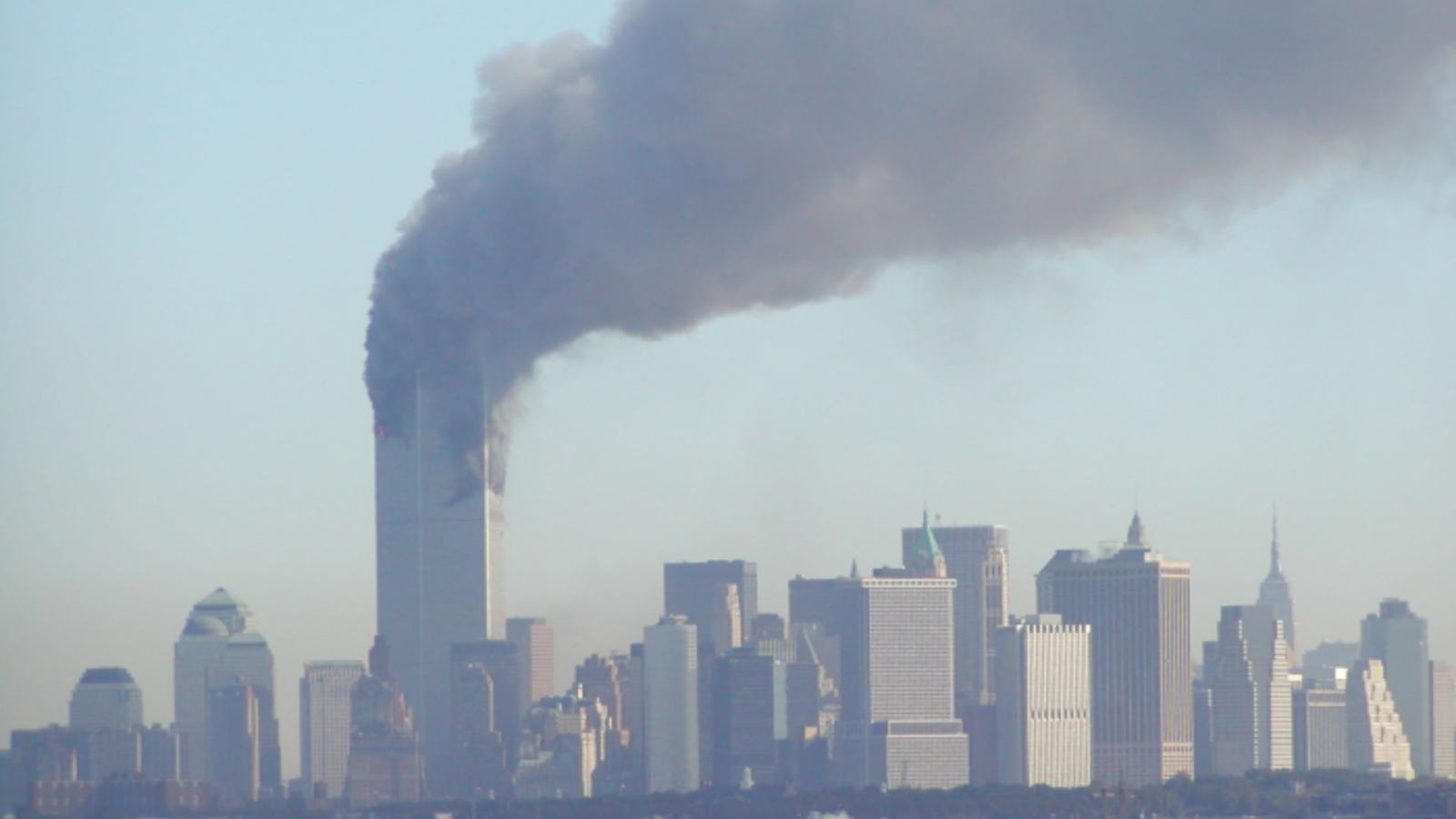 NYC skyline view from East River with thick gray smoke streaming from the top half of both Twin Towers