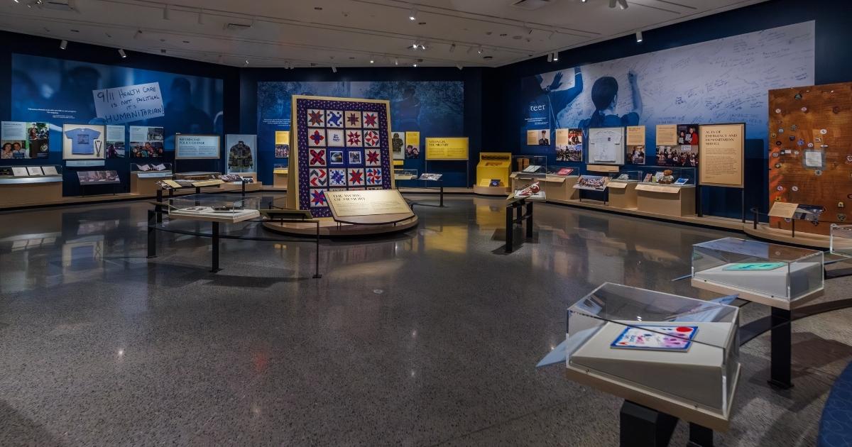 Panorama of exhibition space with various artifacts visible; a quilt is at the center