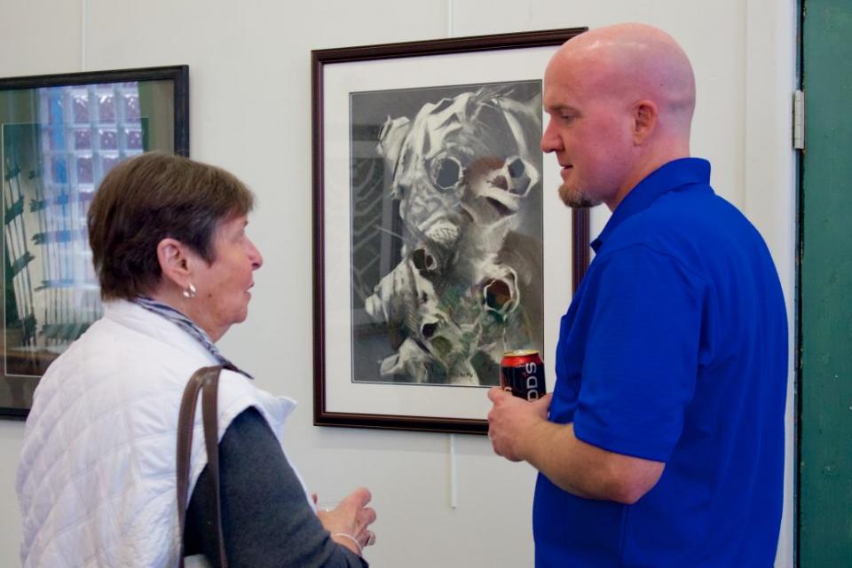 Matthew Tyree, a 9/11 responder and artist, speaks to a woman as the two of them stand beside his framed drawings in an art gallery.