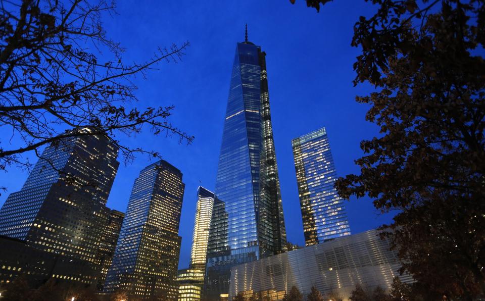 One World Trade Center towers over Memorial plaza at night. The lights of the skyscraper and surrounding buildings shine against the dark blue twilight sky.