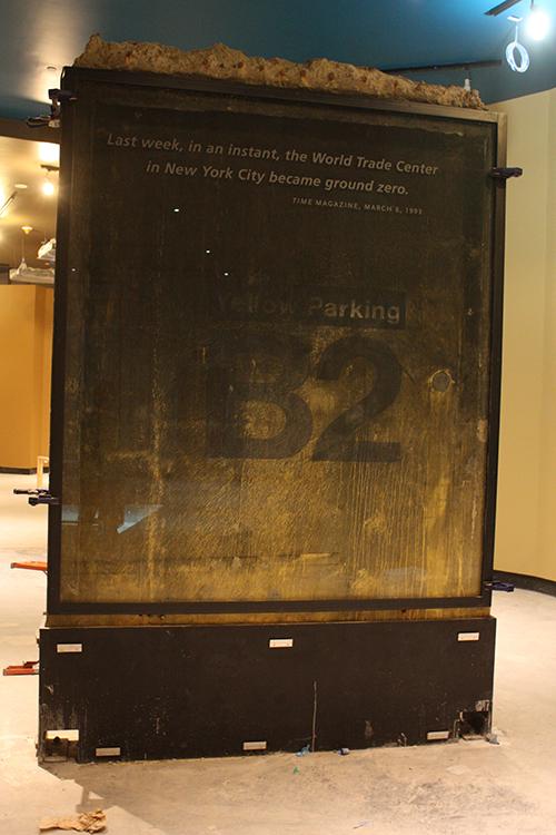 A wall fragment from the World Trade Center parking garage is displayed at the Museum before its opening. The wall fragment is damaged from the 1993 bombing. The fragment reads, “Yellow Parking B2.”