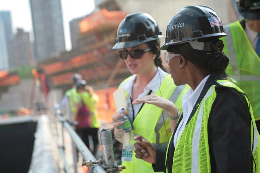 Allison Blais gives a tour of the Memorial pools during the period of construction. She and another woman, both in yellow vests and hardhats, speak beside the construction site.
