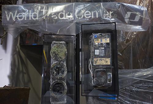 A pay telephone from the 107th floor South Tower observation deck and a signal from a PATH train station are displayed at the Museum before its opening. Both artifacts are heavily damaged.