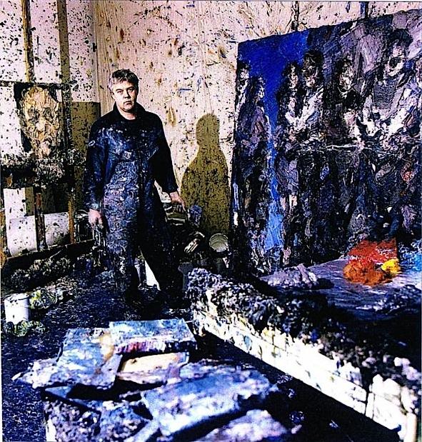 Artist David Stern stands next to his piece “The Gathering” at his studio. Paint is splattered on the walls and floor around him.