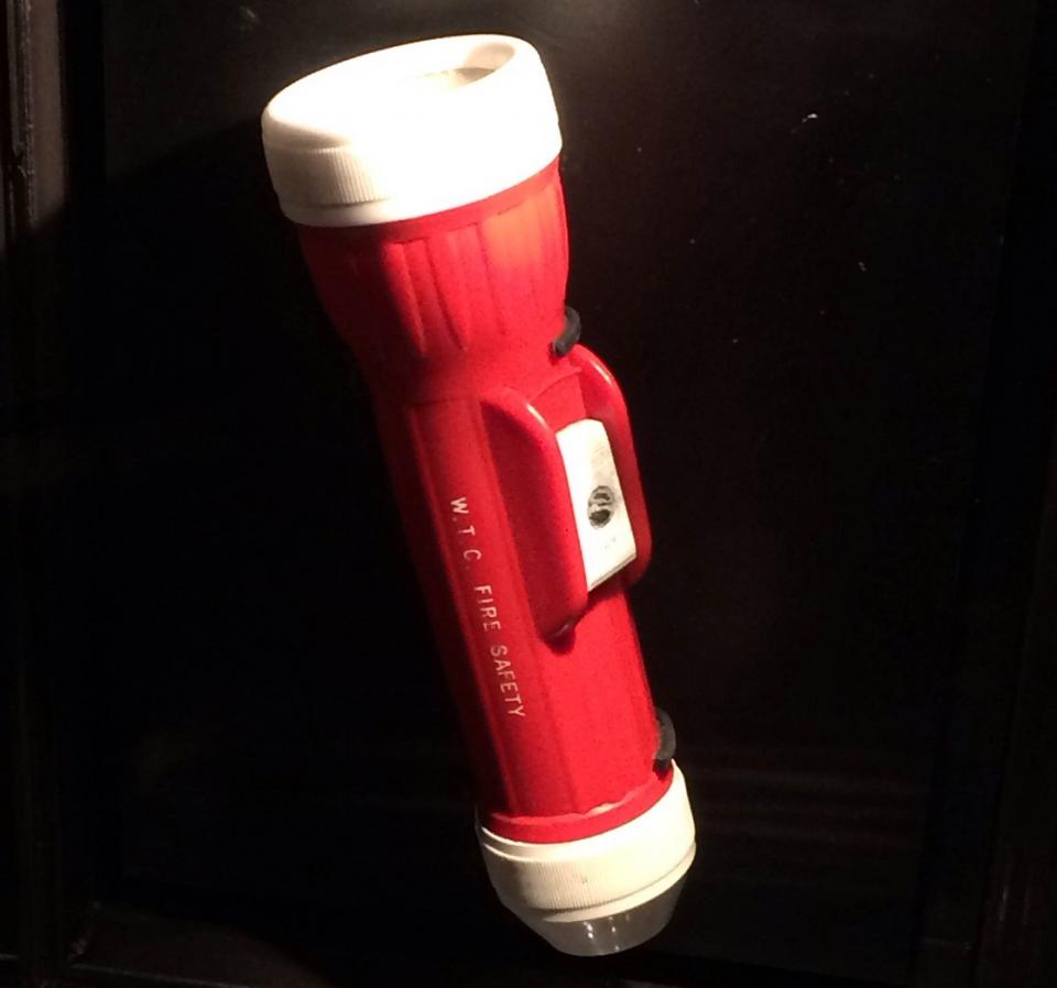 A red and white flashlight used by survivors on 9/11 is displayed on a black surface at the Museum.