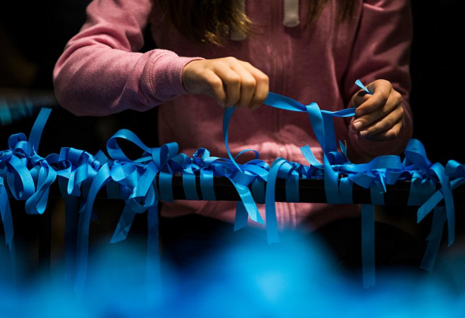 A girl in a pink sweatshirt ties a blue ribbon on a railing surrounding the Last Column. Dozens of other blue ribbons have already been tied on the railing.