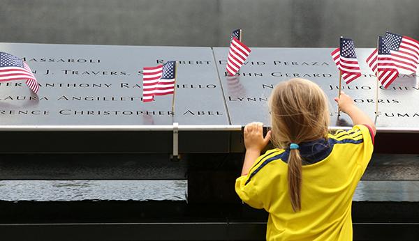 A young girl places an American flag at the names of victims on the bronze parapets at the 9/11 Memorial.
