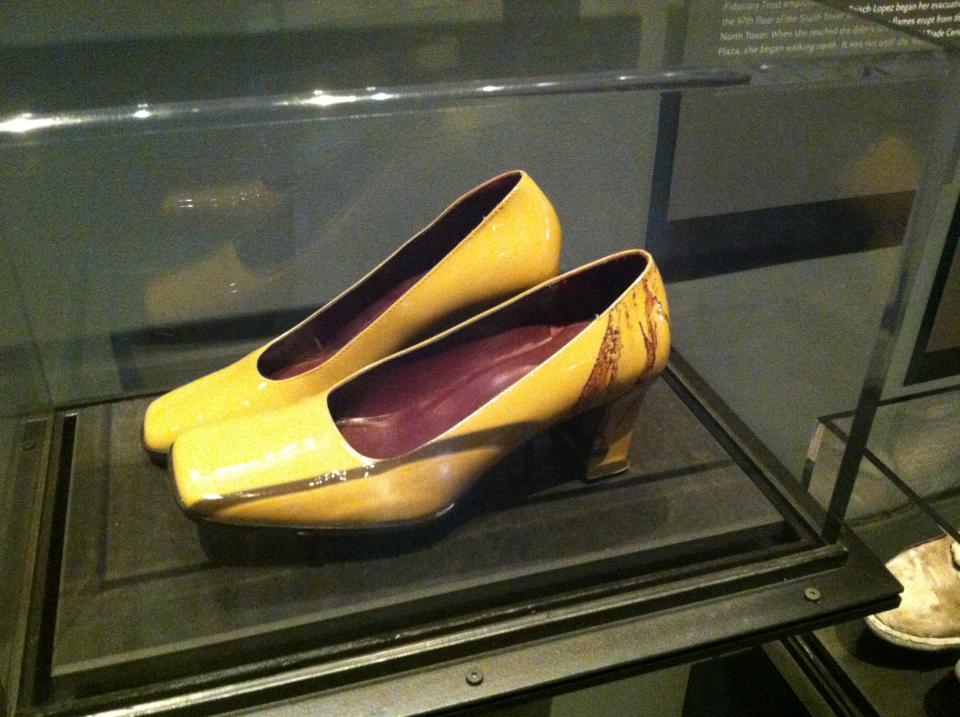 Two yellow high-heeled shoes belonging to Linda Raisch-Lopez are displayed in a glass case at the Museum. Dried blood is visible on the heel of the left shoe.