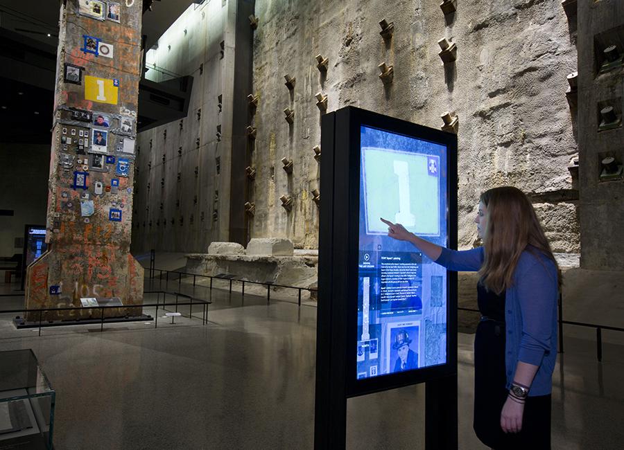 A woman uses an interactive touchscreen near the Final Column in Foundation Hall. The slurry wall towers over her right shoulder.