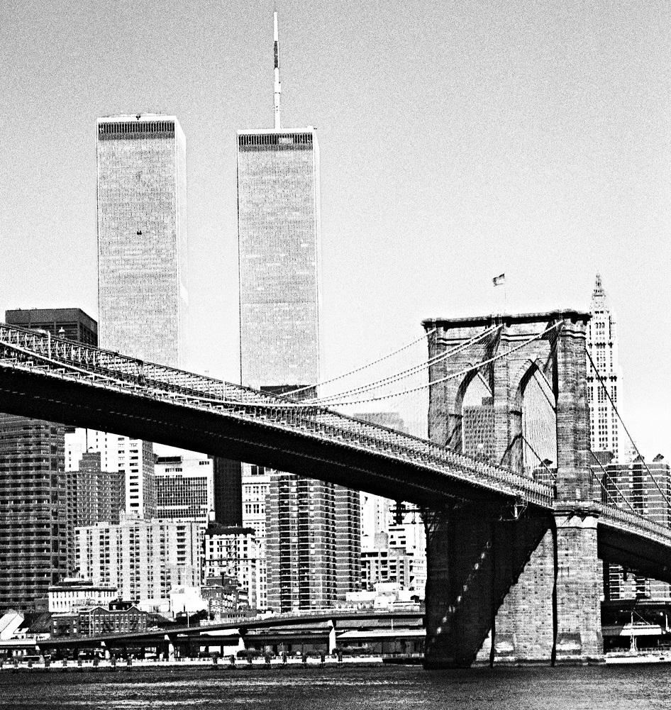 This black-and-white photo shows the newly built Twin Towers rising above lower Manhattan. The Brooklyn Bridge is in the foreground.