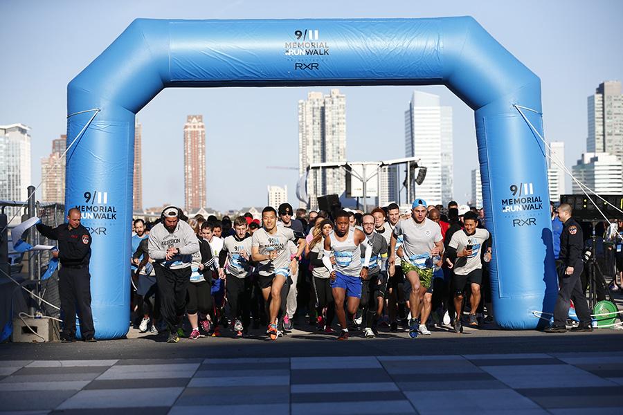 Participants in the fourth annual 5k Run/Walk and Community Day begin running at the blue starting line arch. Jersey City is visible in the background.