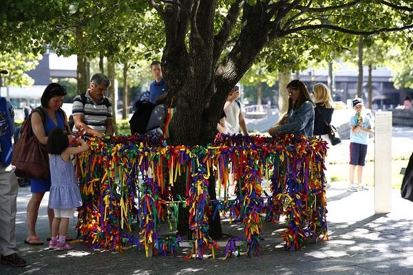 Visitors to the 9/11 Memorial place rainbow colored ribbons on a railing surrounding the Survivor Tree.