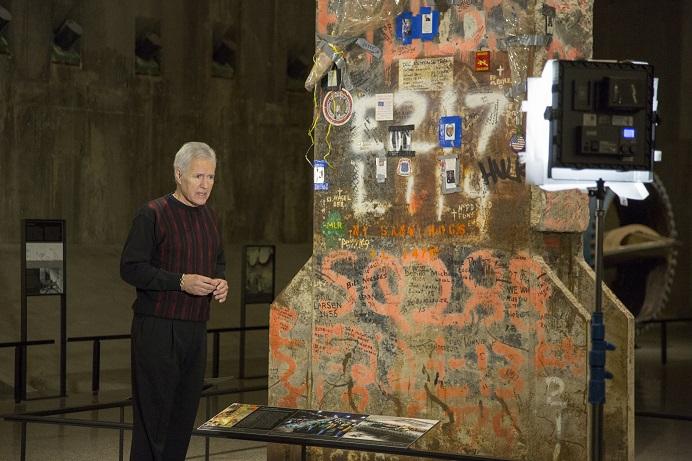 “Jeopardy!” host Alex Trebek stands beside the Last Column as he films part of his show there. The column towers over Trebek and is adorned with photos and other tributes.