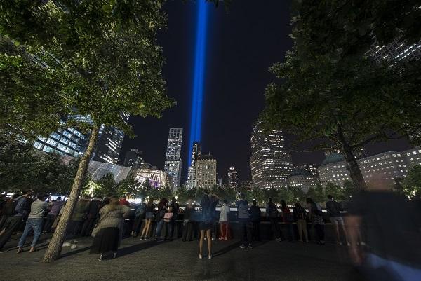 Visitors watch the twin beams of the Tribute in Light as they stand beside the north pool of Memorial plaza.
