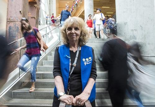 Inez Robertson, a Museum volunteer, poses on steps at the Museum as visitors walk by, going up and down the stairs.