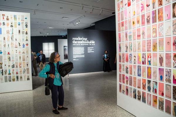 Visitors walk through “Rendering the Unthinkable,” an exhibition of artwork by 13 artists and their reactions to the events of 9/11. Hundreds of pieces of artwork are seen mounted on the walls of the exhibition as one woman looks on in the foreground. 