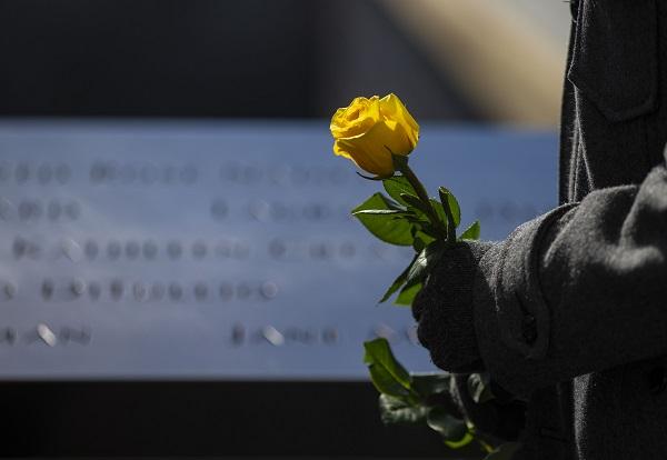 Only a person’s gloved hands are visible as they hold a yellow rose beside names on the 9/11 Memorial.