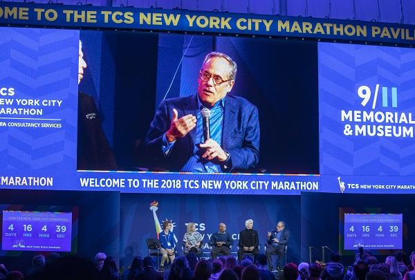 Clifford Chanin, the executive vice president and deputy director for Museum Programs, sits onstage with New York City Marathon athletes at a special public program. The event is projected on a large screen above them.