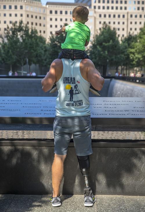 A veteran holds a young boy on his shoulders as he stands beside a reflecting pool at the Memorial.