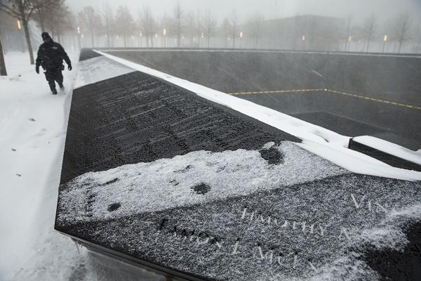An officer trudges through the snow during the height of a winter storm at Memorial plaza. The bronze parapets and walkways at the Memorial are covered in snow.