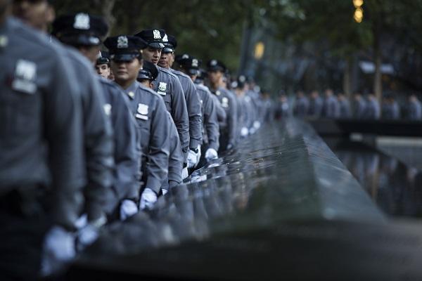 Dozens of formally dressed NYPD recruits are seen lined up in formation beside the south pool of the Memorial.