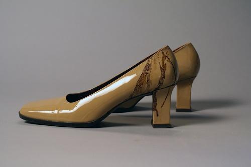 Linda Raisch-Lopez’s yellow, high-heeled shoes are displayed on a gray surface at the Museum. The ankle area of the left shoe is stained with dried blood.