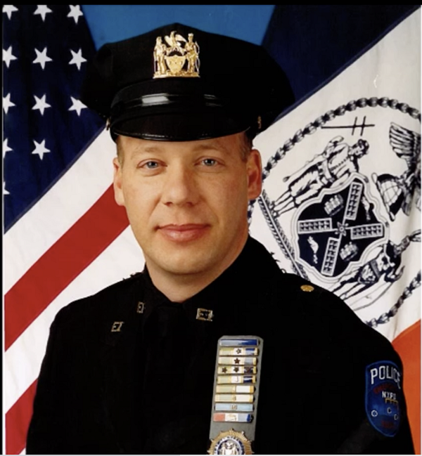 NYPD Detective Scott Strauss poses in his NYPD uniform for a formal photo in front of the American and New York City flags.