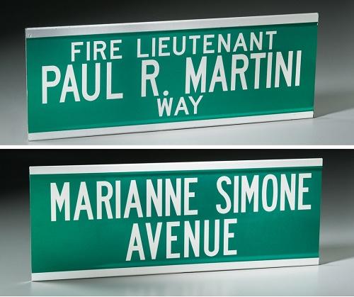 Two street signs memorializing 9/11 victims are displayed on a gray surface at the Museum. One reads Fire Lieutenant Paul R. Martini Way and the second reads Marianne Simone Avenue.