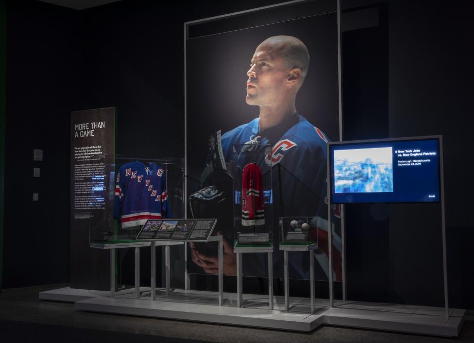 A large photo of Rangers captain Mark Messier is mounted at the exhibition, Comeback Season: Sports After 9/11. Jerseys and other sports artifacts are displayed in front of the photo of Messier.