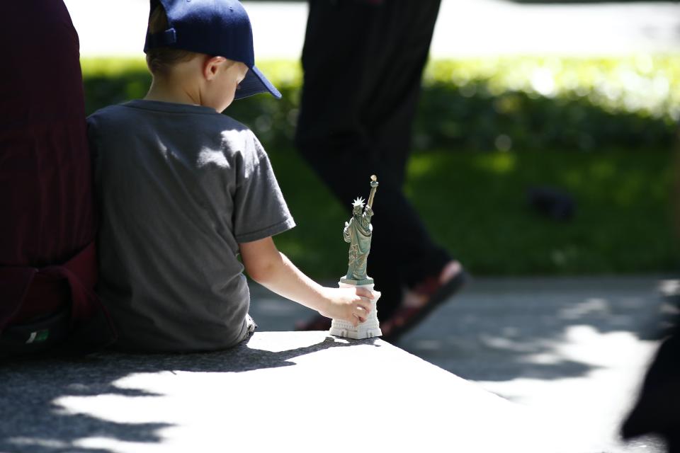 A young boy in a baseball cap plays with a toy model of the Statue of Liberty as he sits at the 9/11 Memorial.
