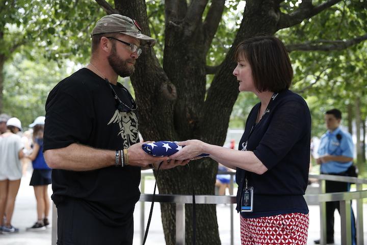 U.S. Army veteran Josh Collins and 9/11 Memorial Museum staff member Heidi Hayden grasp a folded American flag beside the Survivor Tree on Memorial plaza.