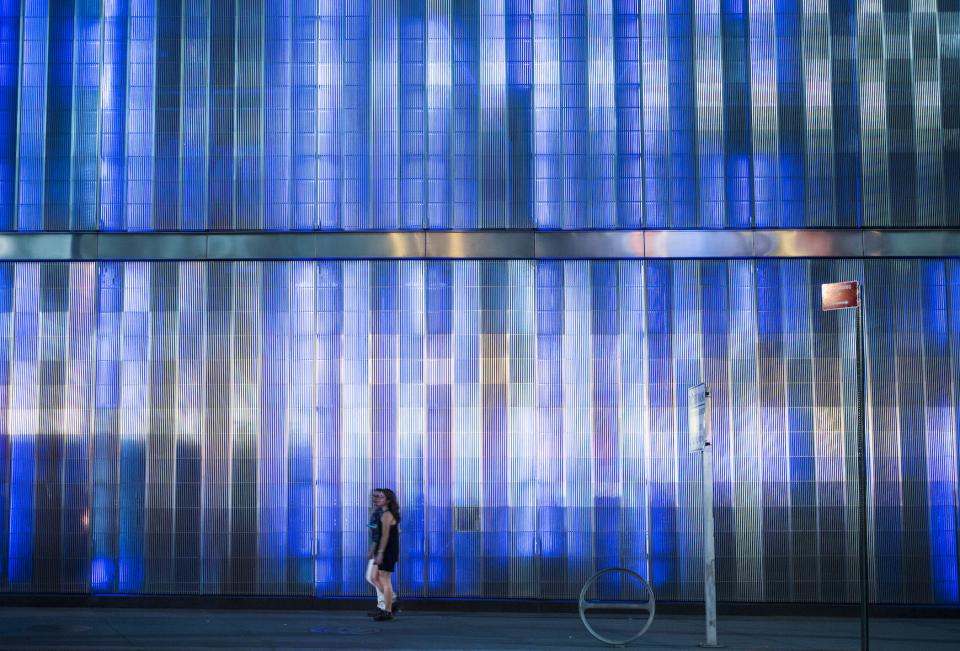 Two people walk by the blue and white facade of 7 World Trade Center in this nighttime shot.