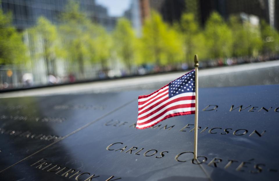 A small American flag stands at a name on a bronze parapet at the 9/11 Memorial.