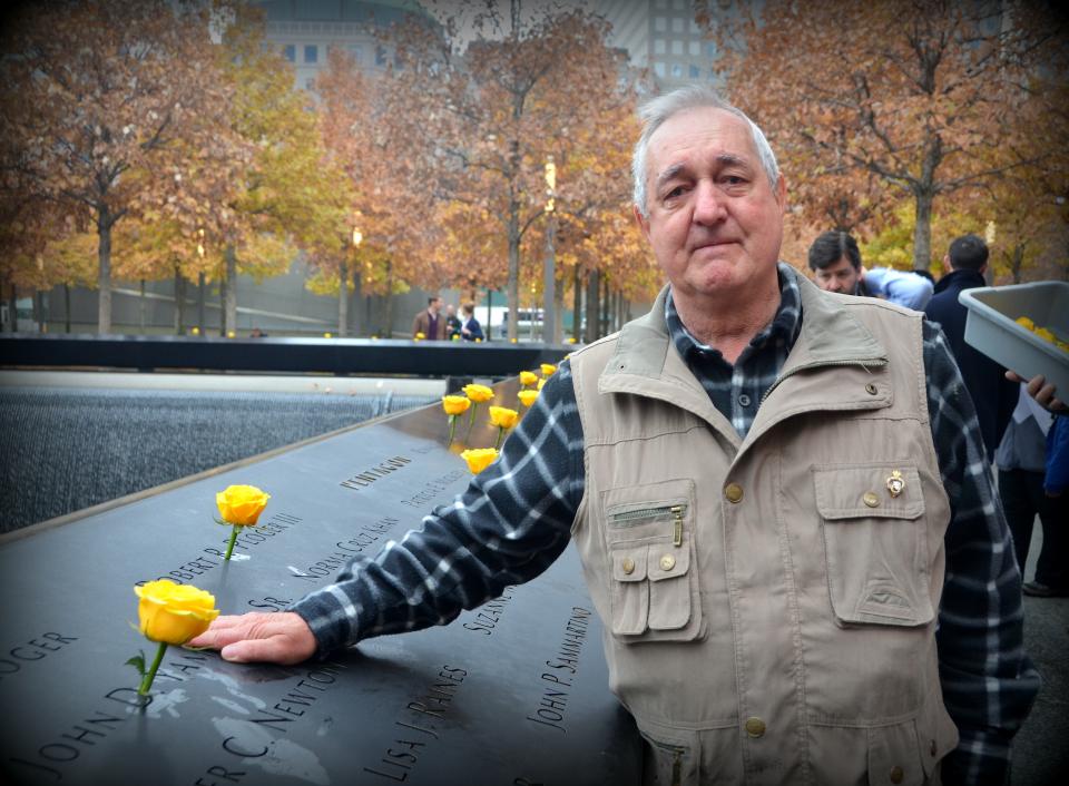 Eric Brown, a former veteran, places a yellow rose on a bronze parapet at the 9/11 Memorial plaza. The fall-colored leaves of the plaza’s swamp white oaks stand in the background.
