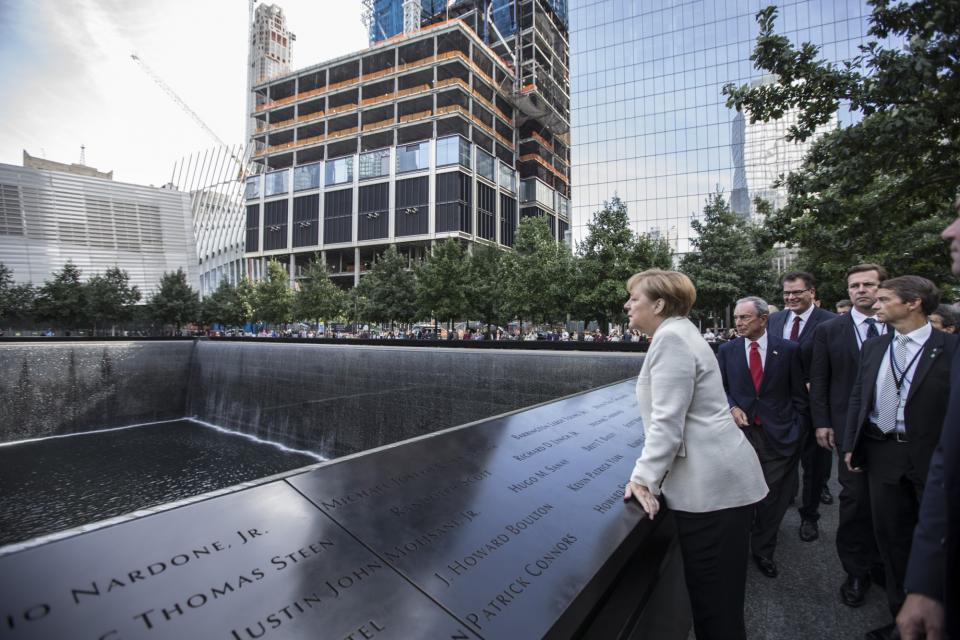 German Chancellor Angela Merkel looks over the south pool at the 9/11 Memorial. Michael Bloomberg and other visitors stand beside her.