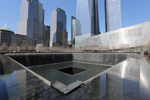 One of the Memorial’s waterfall pools is seen on a sunny, cloudless day in winter. The Museum pavilion, One World Trade Center, and other World Financial Center buildings are in the background.