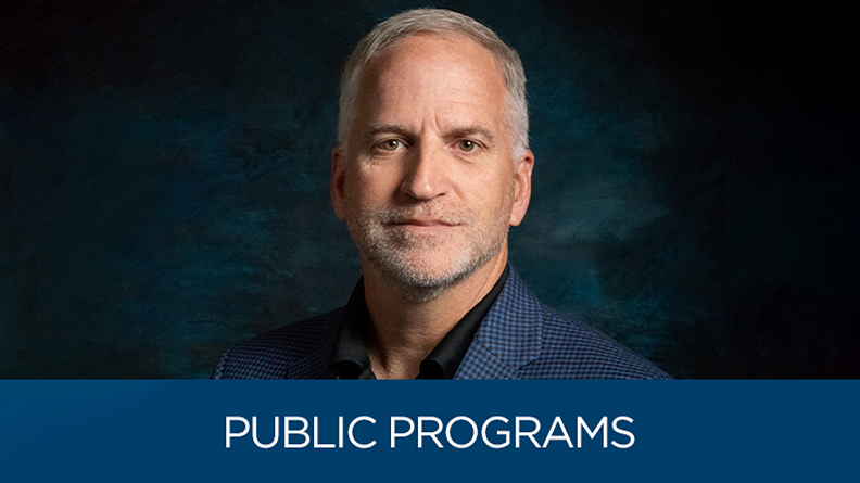 A man in a navy blue sport coat sits for a professional headshot in front of a dark background. At the bottom are the words "Public Programs."