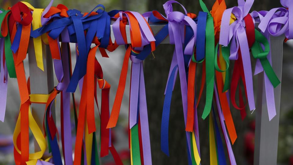 Dozens of rainbow-colored ribbons are tied around a metal post.