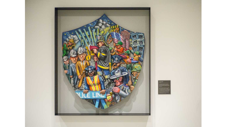 Enamel on epoxy sculpture by Red Grooms titled The Shield. The large piece is designed in the shape of a shield with a three dimensional collage of characters rendered with cartoon-like appearances and painted in bold colors.