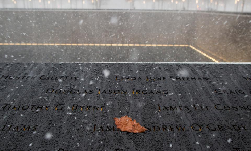 Snow falls on the 9/11 Memorial while a yellow leaf rests on the bronze parapets. 