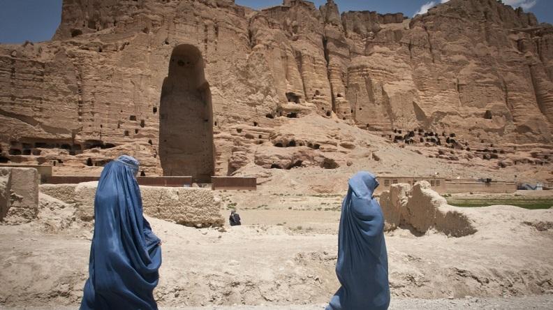 Two women in blue burkas walk past the huge cavity where one of the ancient Buddhas of Bamiyan, known to locals as the "Father Buddha," used to stand, June 17, 2012.