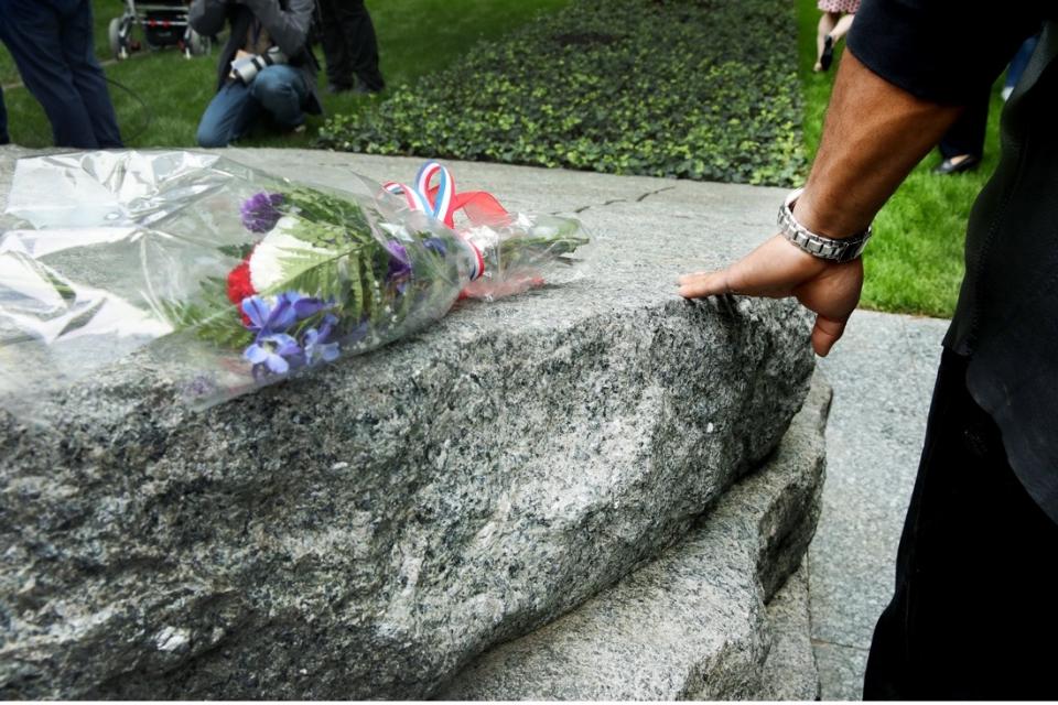 A bouquet of flowers is placed on the Memorial Glade while an onlooker stands on the right.